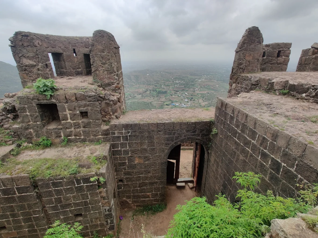 win temple spires and triangular stone ramparts rising above rain‑filled ponds, set against the Bhuleshwar range under a clear morning sky