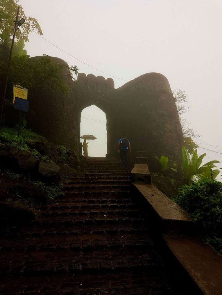 The misty stone gateway of Sinhagad Fort, as trekkers approach in the early morning.