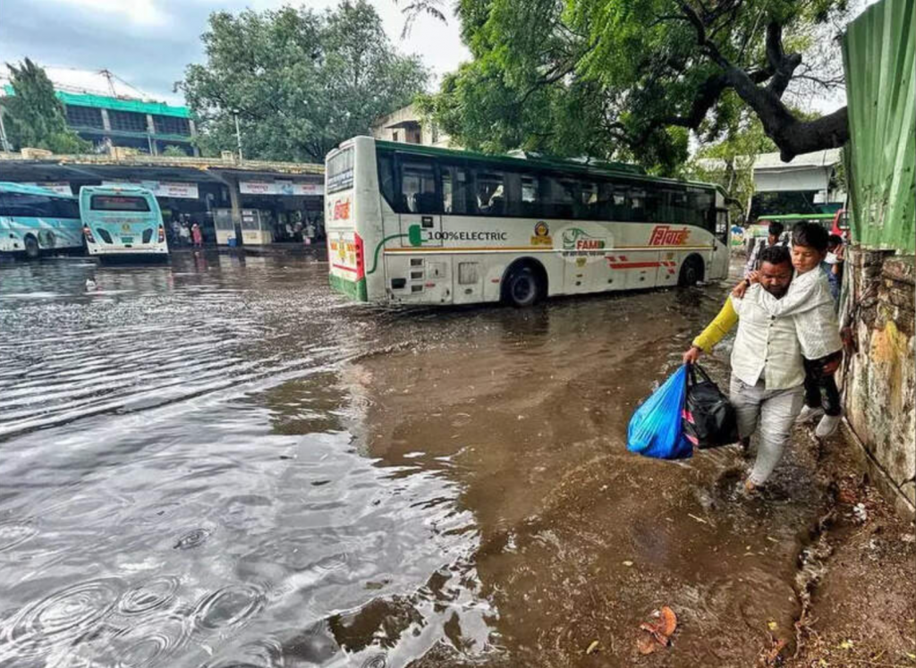 Commuters wading through ankle‑to‑knee‑deep water at Swargate bus depot during a brief pre‑monsoon rain