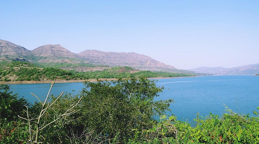 Reservoir of Mulshi Dam reflecting verdant Sahyadri hills under a cloudy sky.