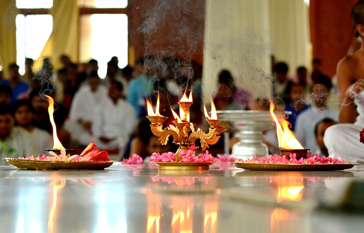 Neighborhood residents in traditional attire distributing modaks and lighting diyas along a decorated street lined with Ganesh mandals.