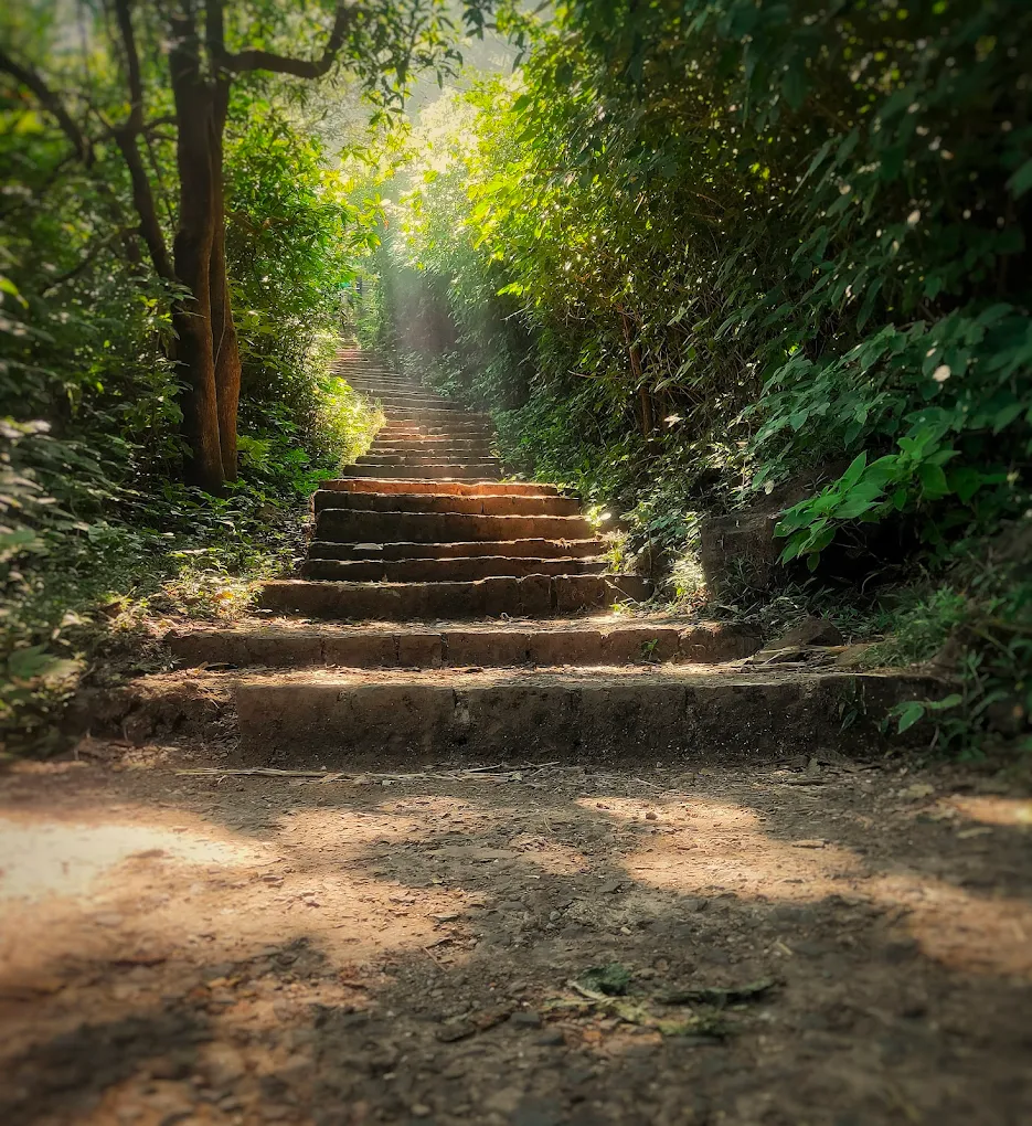 A circular stone rampart enclosing two mirror‑like lakes and temple ruins, rising above verdant foothills and overlooking Aamby Valley