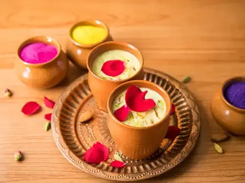 Glasses of chilled thandai and plate of golden gujiyas arranged on a festive Holi platter.