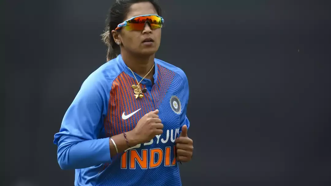 Veda Krishnamurthy walking off cricket field during sunset, bat raised, farewell moment