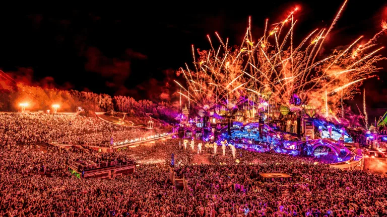 People watching the Tomorrowland 2025 livestream on a large screen at home with colorful lighting and party atmosphere.