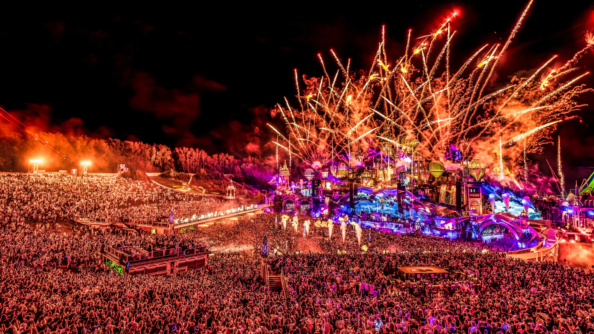 People watching the Tomorrowland 2025 livestream on a large screen at home with colorful lighting and party atmosphere.